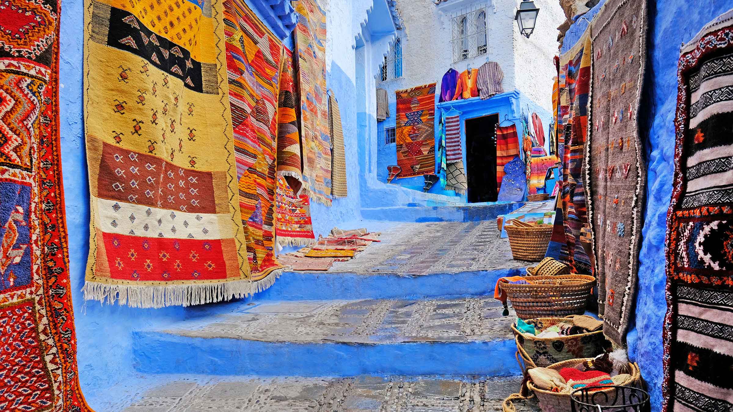 Traditional rugs and handcrafted textiles hanging in a vibrant alley in Morocco
