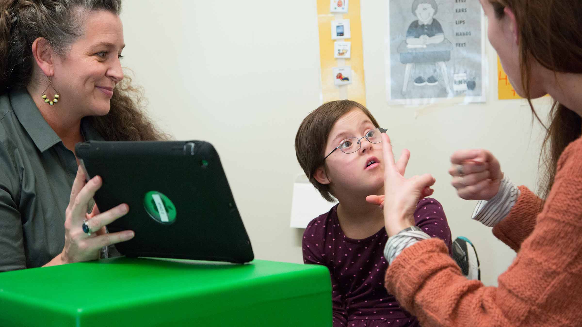 Child participates in a communication therapy session with an instructor and student using sign language and a tablet