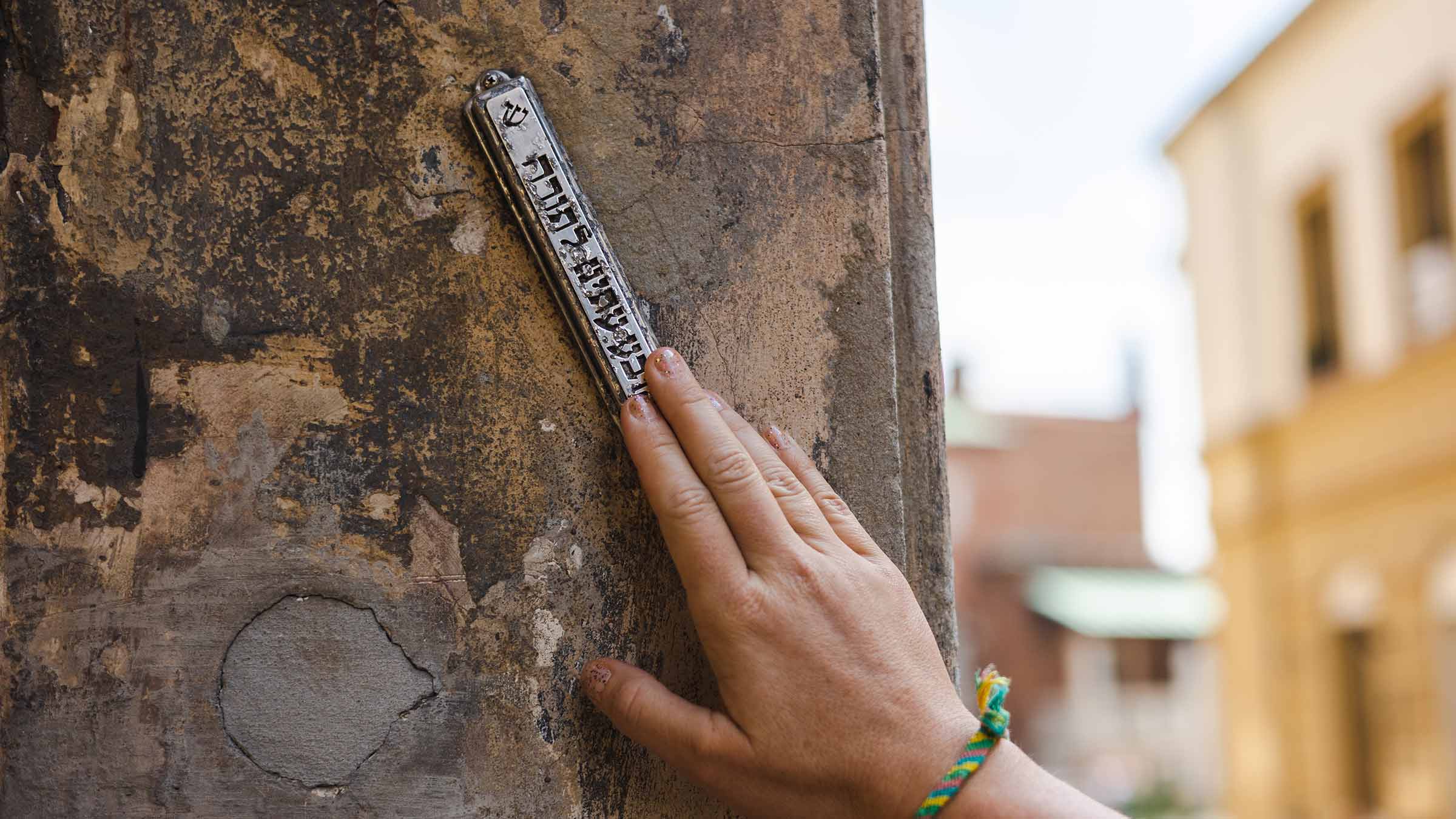 Hand reaching up to touch a mezuzah at the entrance of a house