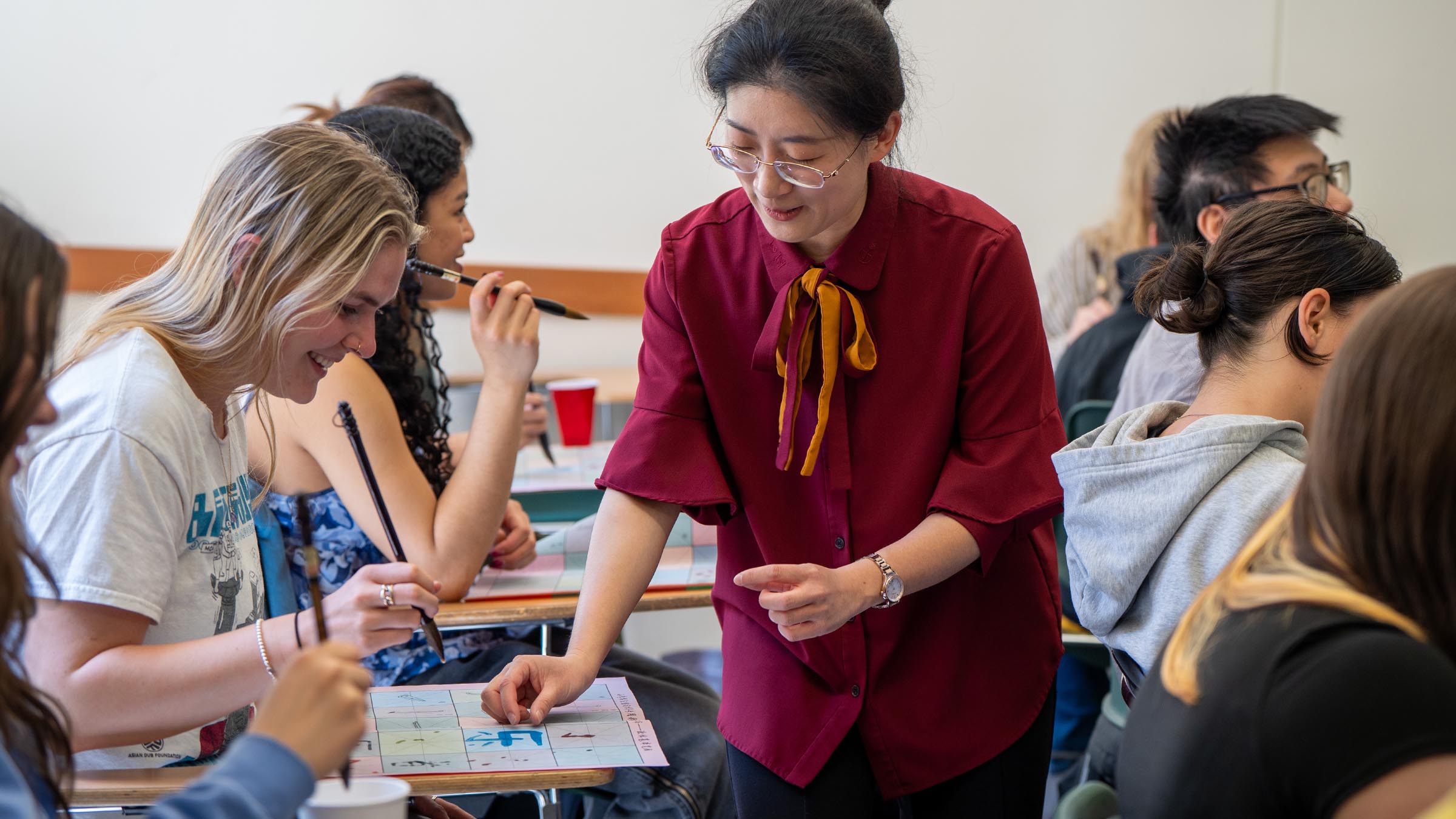 Instructor guiding students as they practice calligraphy using a traditional brush