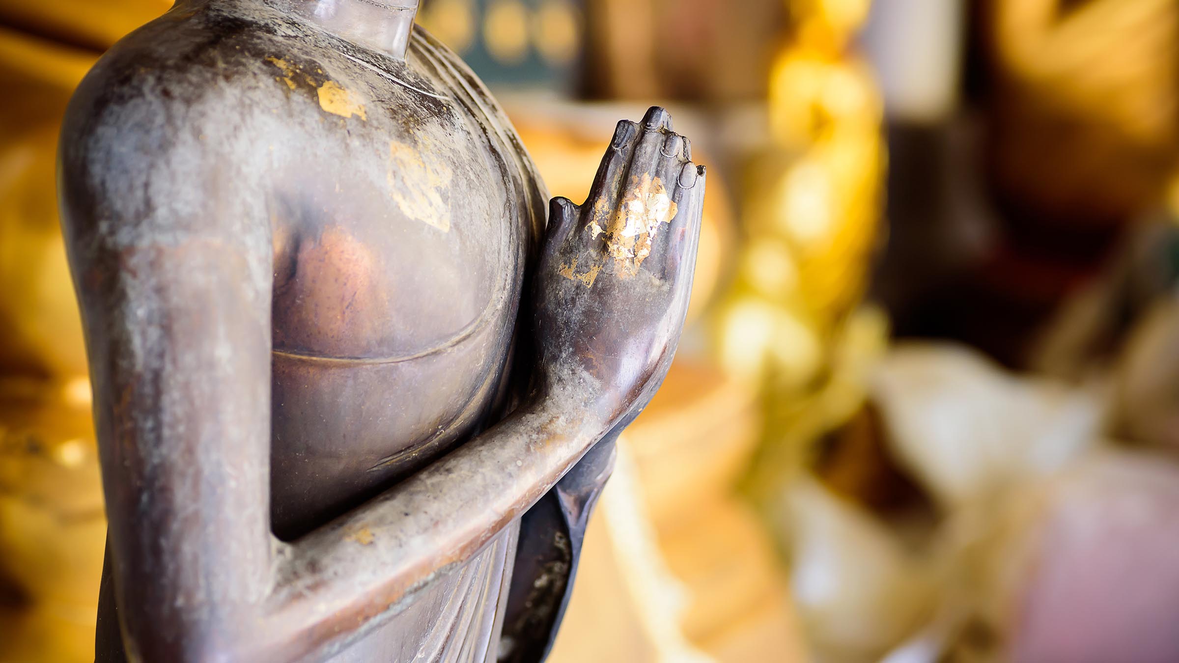 Close-up of a Buddha statue with hands pressed together in a gesture of reflection and gratitude